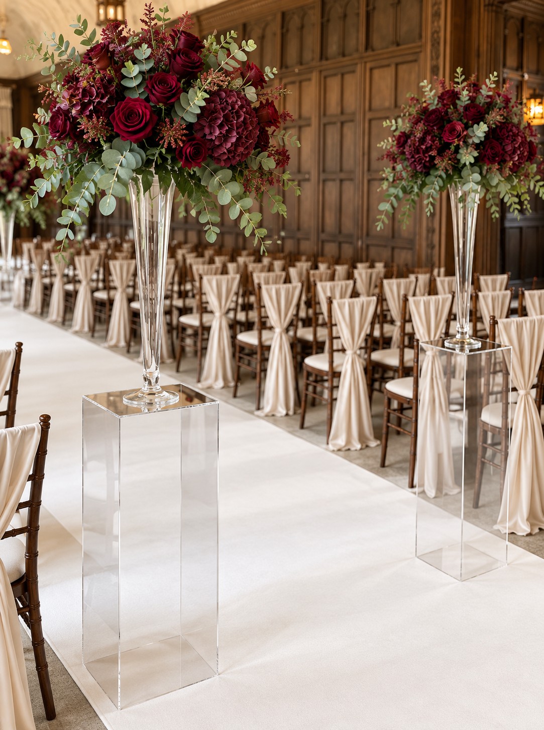 80 cm clear Perspex acrylic plinth styled with a tall trumpet vase, burgundy flowers and champagne wedding chair sashes