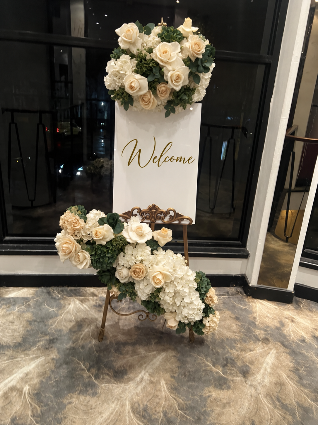 Real event setup with a centred Welcome sign on an ornate gold easel and ivory floral arrangements